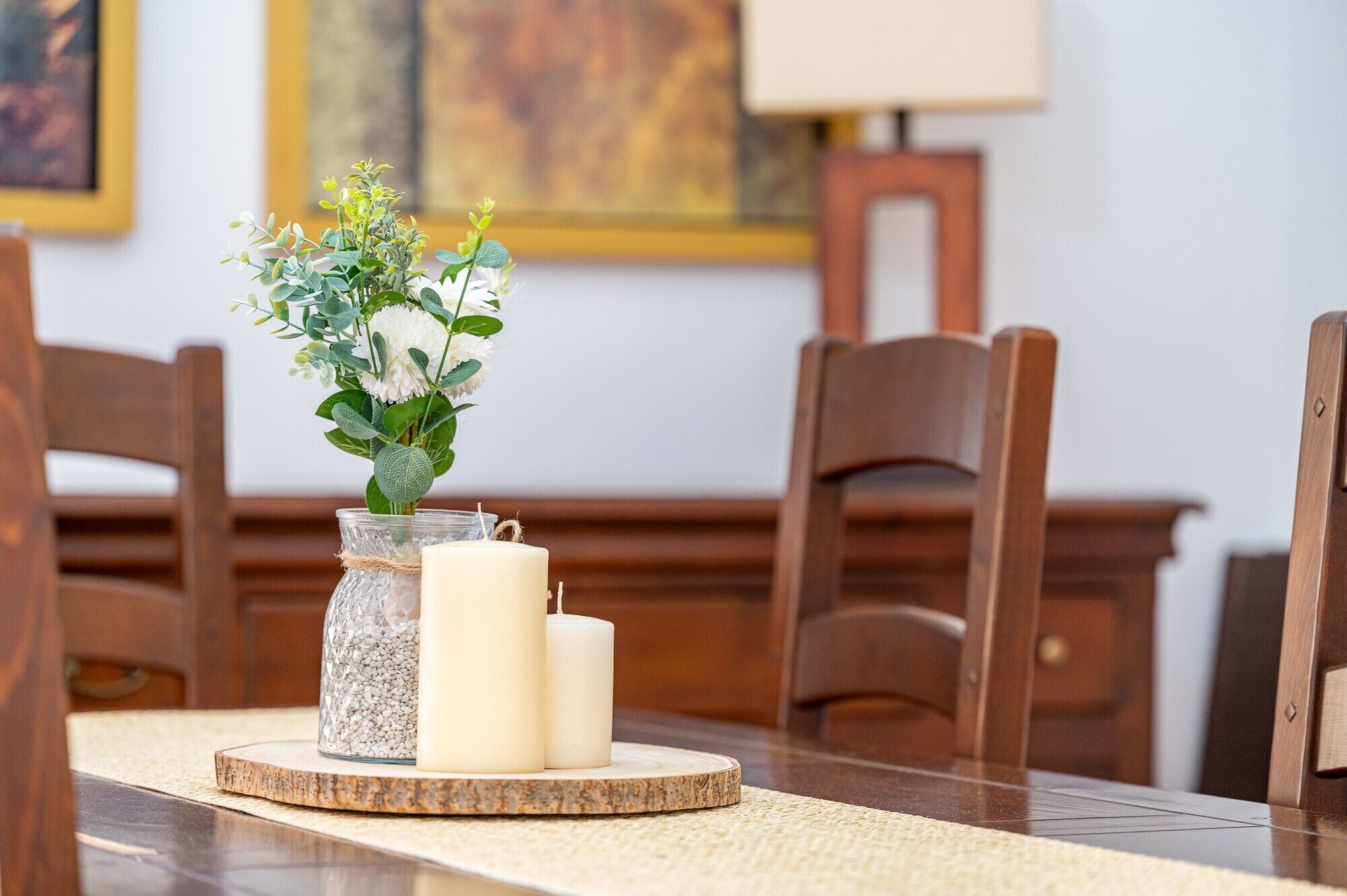 Une table à manger ornée d’un bocal en verre contenant des petits galets blancs, de deux bougies blanches et d’un arrangement floral.