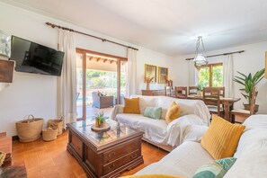 A cozy living room with a sofa, a coffee table, and a TV mounted on the wall. - Can Calistro: Rural Villa with Private Tennis Court (Selva)