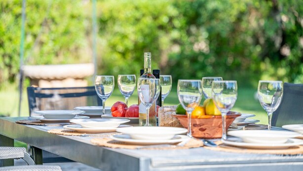 An outdoor dining table set with plates, glasses, and a bottle of wine, surrounded by greenery. - Can Calistro: Rural Villa with Private Tennis Court (Selva)