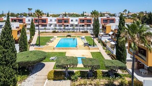 Un hotel moderno con una piscina central, rodeado de céspedes cuidados y palmeras.