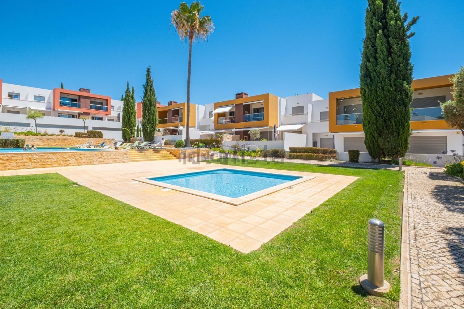 Ein moderner Wohnkomplex mit Schwimmbad, gepflegten Rasenflächen und blauem Himmel.