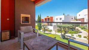 Un balcón con vista a una zona residencial, una silla, una mesita y una chimenea de ladrillo.