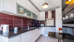 Una cocina moderna con armarios blancos, encimera de granito, pileta de acero inoxidable y horno empotrado.