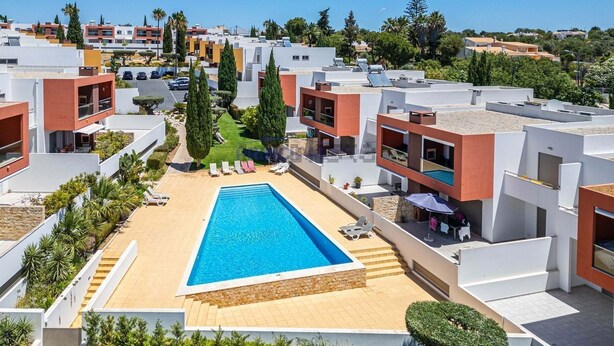 Un moderno complejo residencial con piscina central, rodeado de tumbonas y un jardín bien cuidado.