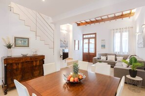 Ein modernes Wohnzimmer mit Esstisch aus Holz, einer Sofagarnitur und einer Treppe.