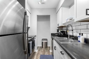 A compact kitchen with a stainless steel refrigerator, a stove, a sink, and a trash bin. - Arlington 3BR | AT&T, Globe Life, 6 Flags, Parking (Arlington)