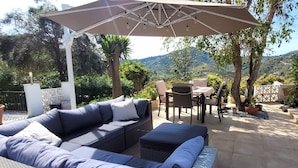 Eine Terrasse im Freien mit einer Eckcouch, einem Esstisch mit Stühlen und einer Pergola darüber.