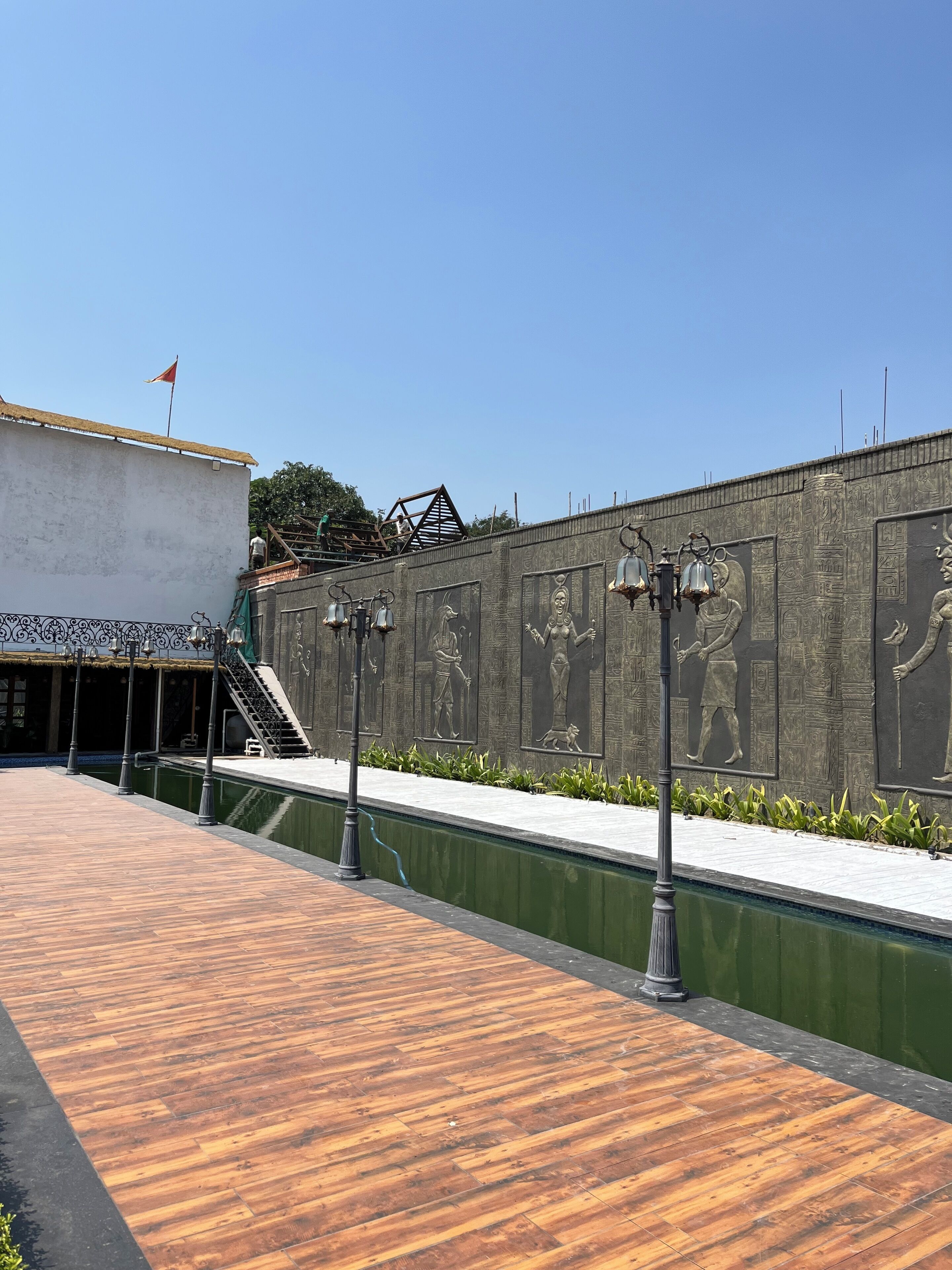 A courtyard with a wooden deck, a wall with Egyptian-style reliefs, and a flag on a building.