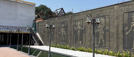 A courtyard with a wooden deck, a wall with Egyptian-style reliefs, and a flag on a building.