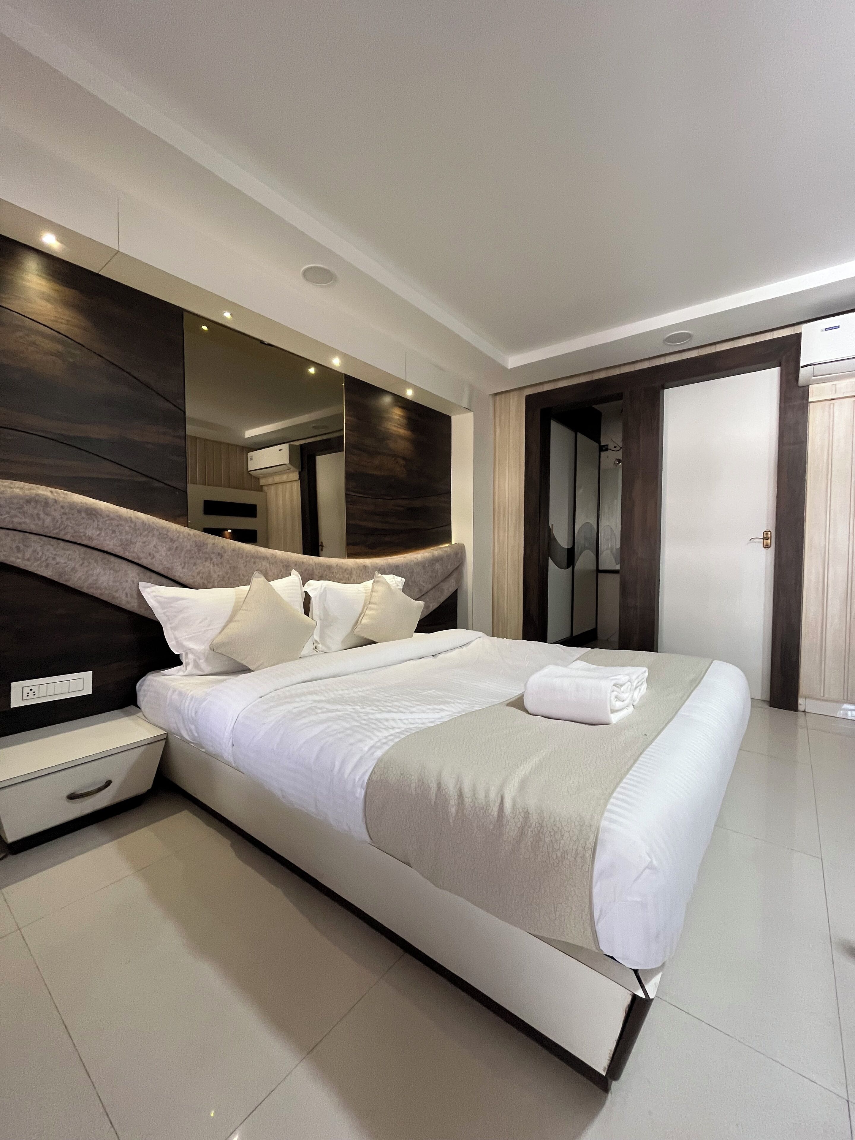 A modern bedroom with a large bed, a bedside table, a mirror, and a wardrobe.