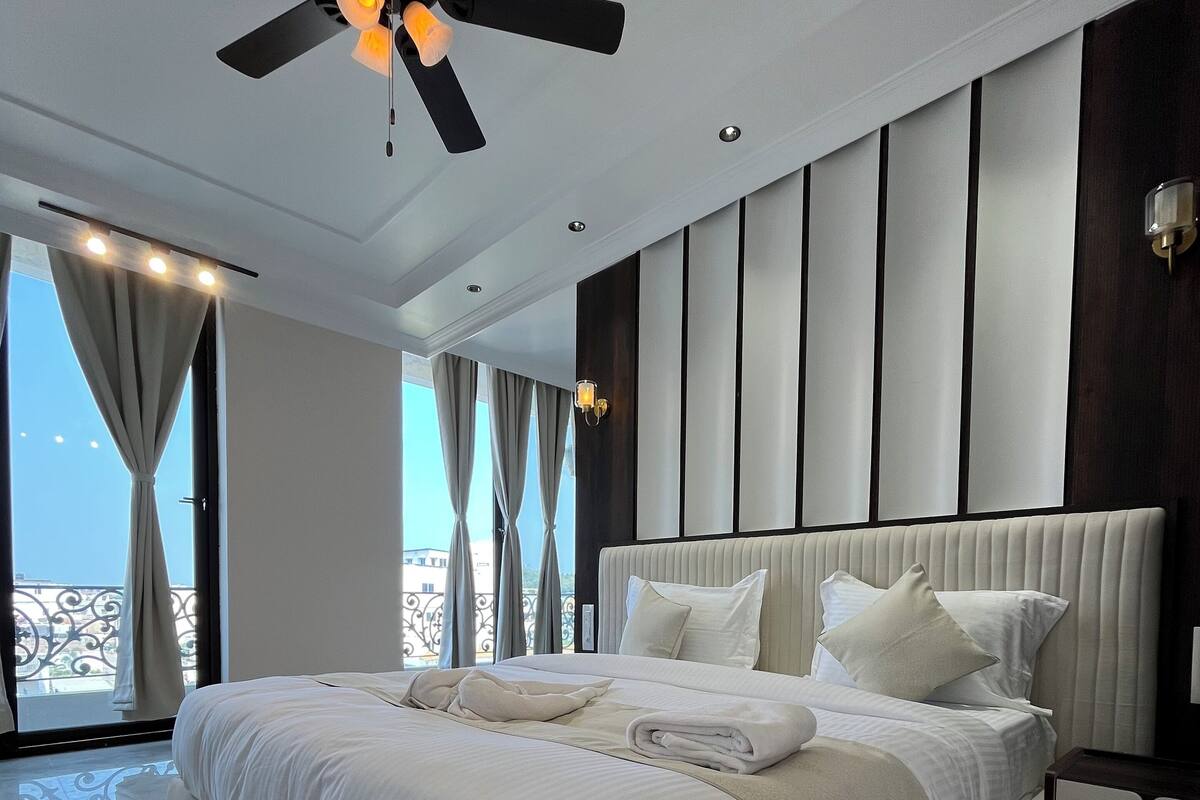 A modern bedroom with a large bed, a ceiling fan, and a balcony with curtains.
