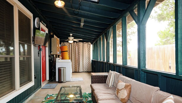 A covered porch with a glass table, a beige sofa, and a ceiling fan.
