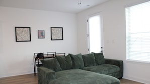 A living room with a green sectional sofa, a dining table with chairs, and two framed artworks on the wall. - The Purrfect Stay—a charming, cat-themed 2.5-bedroom home in Maryville, TN. (Maryville)
