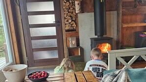 A cozy cabin interior with a wooden interior, a fireplace, a dining table with food, and a child playing.