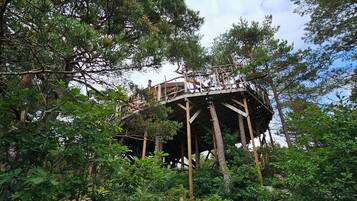 Ein Baumhaus in bewaldetem Gebiet, mit einer Holzplattform und Geländern.