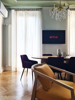 A modern living room with a dining area, a flat-screen TV displaying 'NETFLIX', and a chandelier. - Serendipity Luxury Apartments - Brera (Milano)