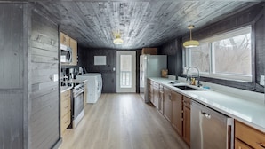A compact kitchen with wooden walls, a central island, and a window providing natural light. - Seneca Lake Barndominium Retreat (Quaker City)
