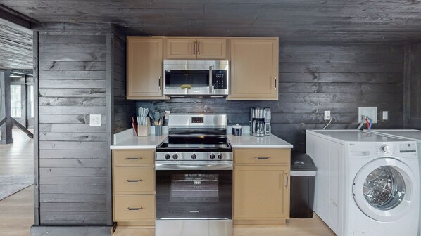Une cuisine compacte équipée d’un four à micro-ondes, d’une cuisinière et d’un four intégrés, ainsi que d’un lave-linge et de meubles de rangement en bois.