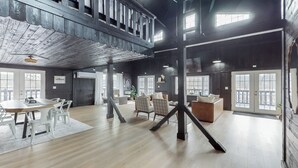 A spacious loft-style room with a high ceiling, exposed wooden beams, and large windows. - Seneca Lake Barndominium Retreat (Quaker City)