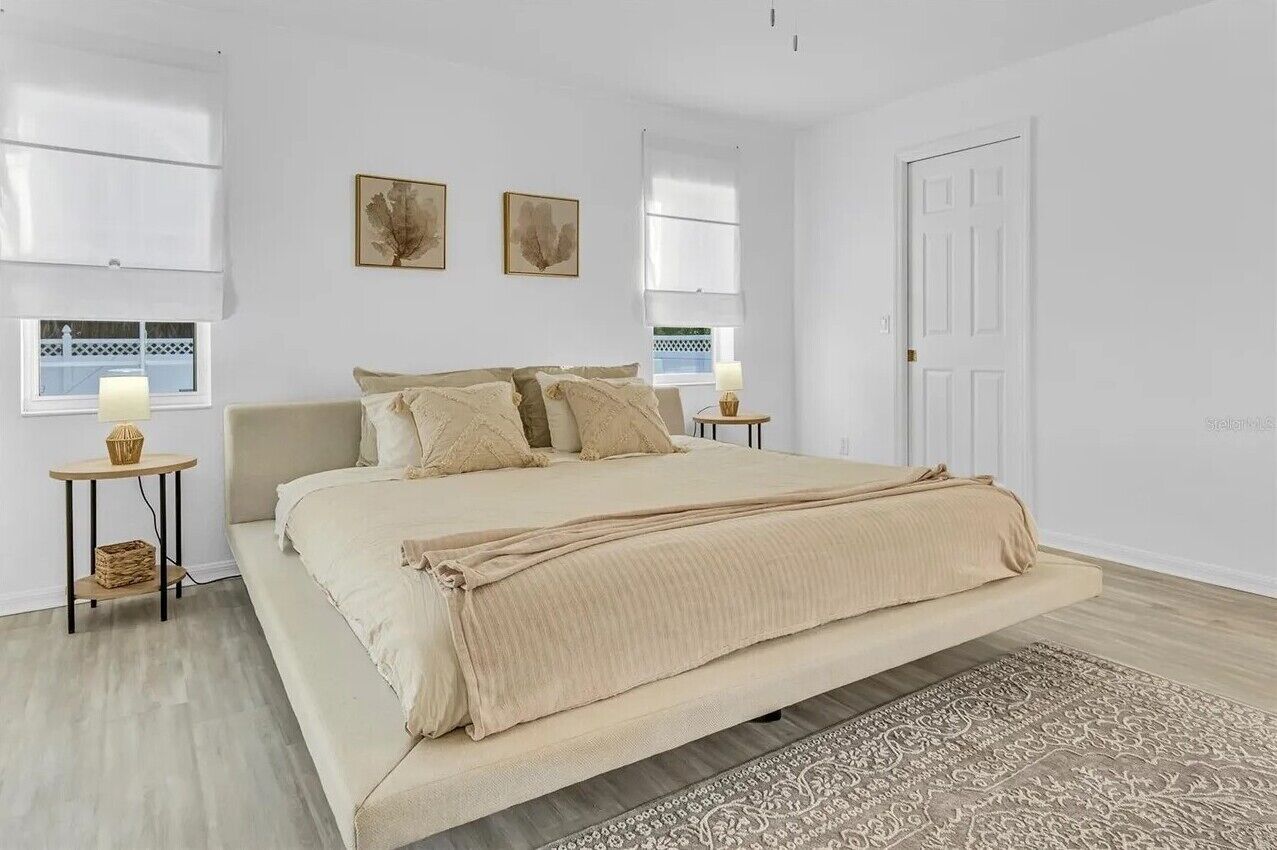 Une chambre à coucher avec un grand lit, deux tables de chevet, une fenêtre donnant sur un beau paysage et une porte.