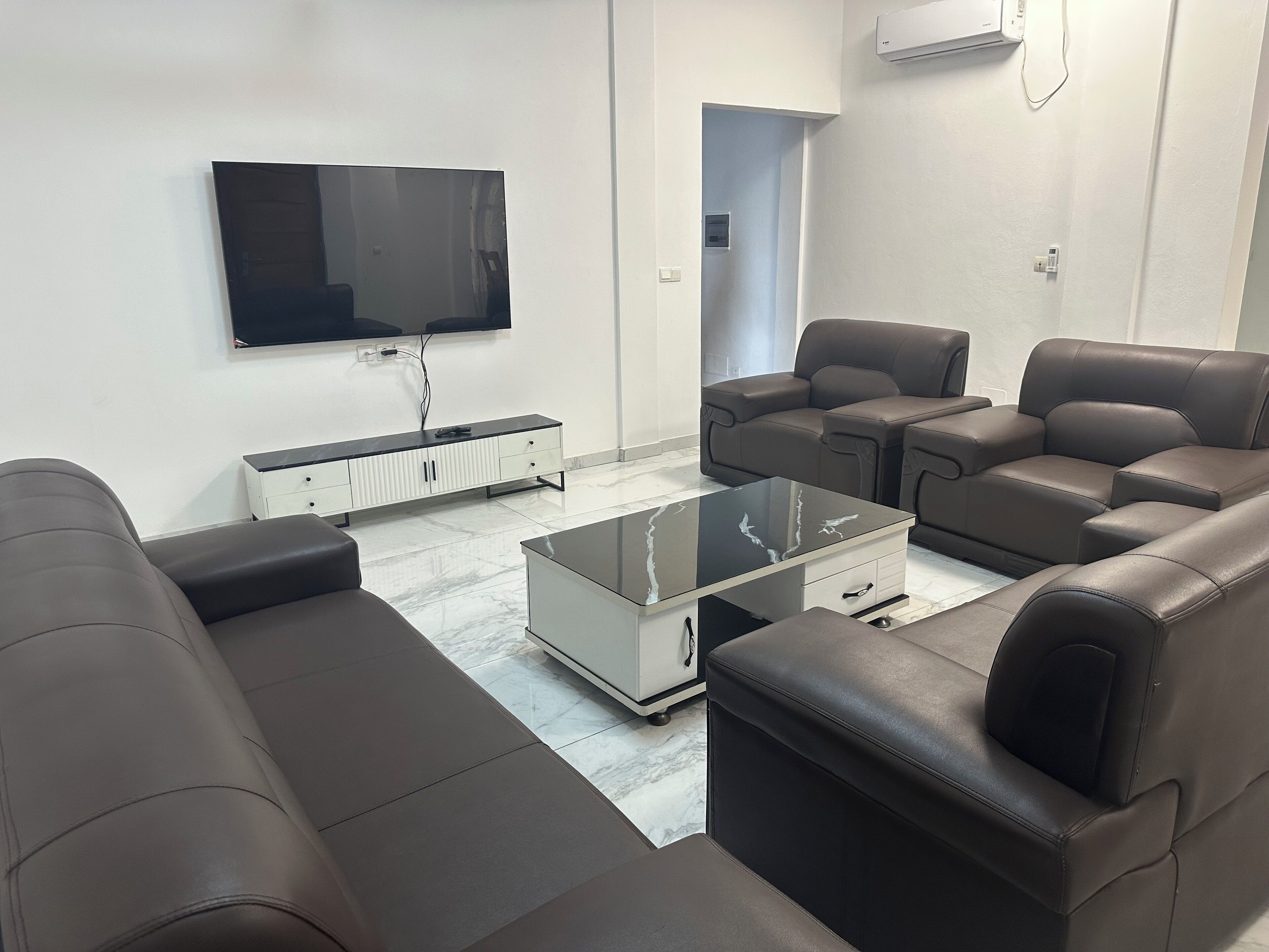 A modern living room with a flat-screen TV, leather sofas, a glass coffee table, and a white cabinet.