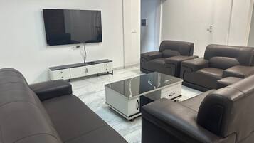 A modern living room with a flat-screen TV, leather sofas, a glass coffee table, and a white cabinet.