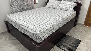 A bed with a checkered bedspread, a dark wooden headboard, and a black textured mat at the foot of the bed.
