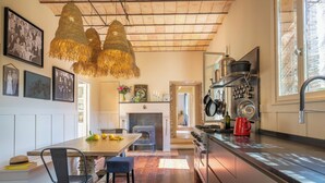 A modern kitchen with a wooden ceiling, pendant lights, a dining area with a table and chairs, and a view of the living area through an open door. - Maison Carei perched on the heights of Menton (Castellar)