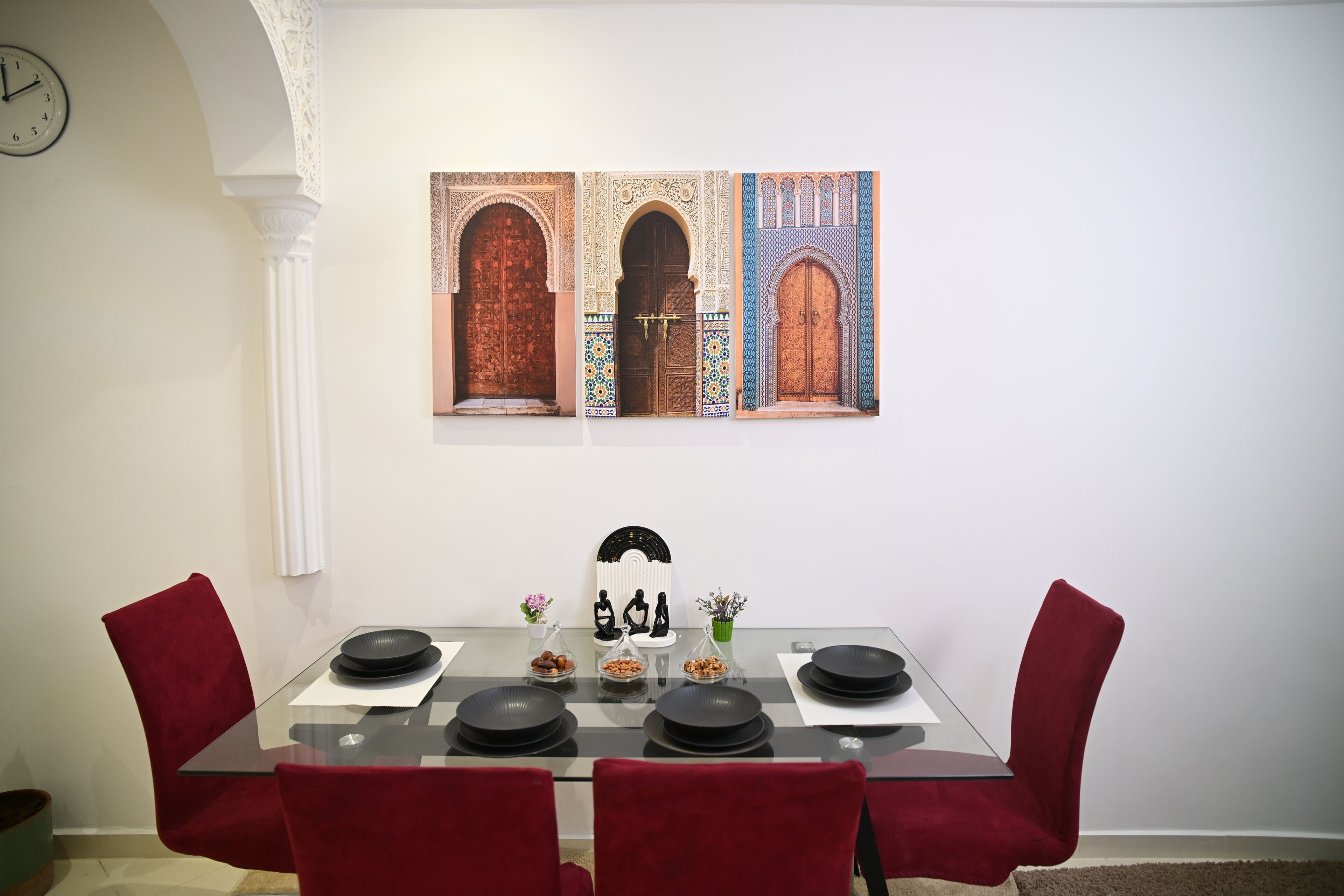 Zona pranzo con tavolo in vetro, sedie rosse e orologio a parete.