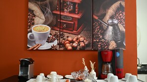 En kaffestation med en kaffebryggare, koppar och en kaffekvarn placerad på ett bord framför en vägg som pryds av en tavla med kaffetema.