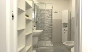 Et moderne badeværelse med glasvægs brusekabine, håndvask og toilet.
