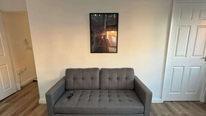 Un divano grigio con un telecomando sopra, un quadro appeso al muro e una porta bianca sullo sfondo.