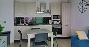 A compact kitchen with a microwave, stove, and a dining area with chairs. - Krystal Palace Appartement proche Monaco (Beausoleil)