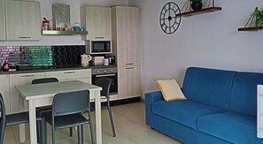 A compact kitchen with a dining table and chairs, a blue sofa, and a wall clock. - Krystal Palace Appartement proche Monaco (Beausoleil)