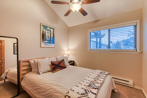 A bedroom with a bed, a ceiling fan, a window with blinds, a nightstand, and a poster on the wall. - Updated Apt | Walking Distance to Ski Shuttle and Dining! (Avon)