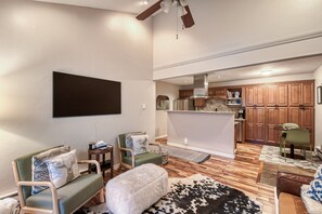 A living room with a flat-screen TV, two green sofas, a white furry ottoman, a black and white cowhide rug, and a wooden dining table with chairs. - Updated Apt | Walking Distance to Ski Shuttle and Dining! (Avon)