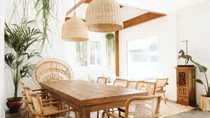 Zona pranzo con tavolo in legno e sedie in vimini, circondata da piante in vaso e un lampadario.