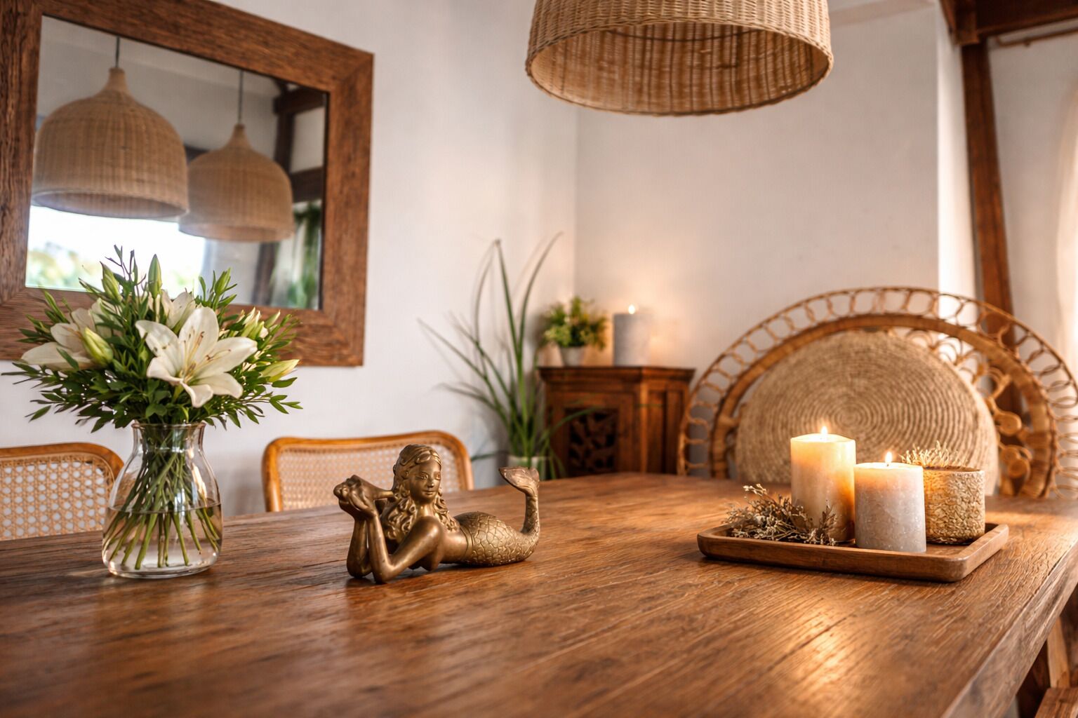A wooden dining table with a vase of flowers, a decorative statue, candles, and woven baskets.