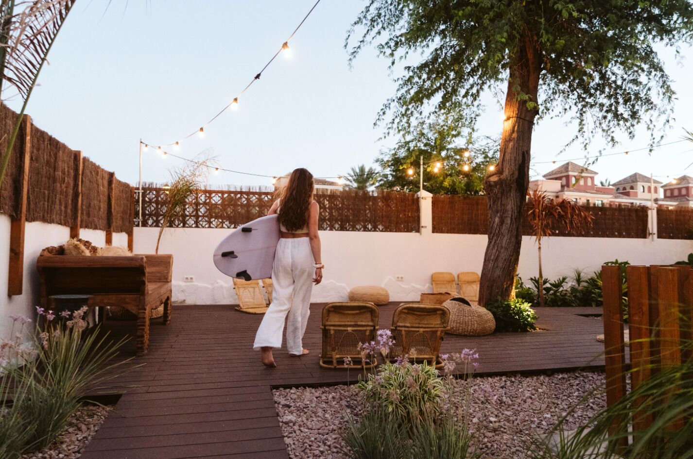 A wooden deck with wicker furniture, a surfboard, and string lights.