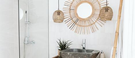 A bathroom with a glass shower enclosure, a wooden vanity with a large bowl sink, and two hanging wicker lamps.