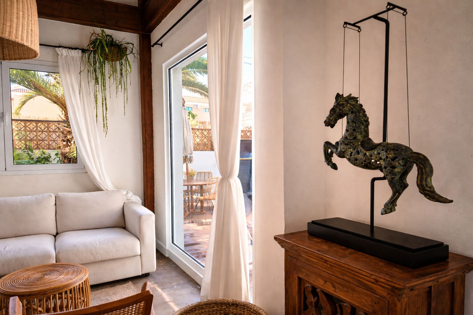 A living room with a sofa, a hanging plant, a wooden cabinet, and a decorative horse sculpture.