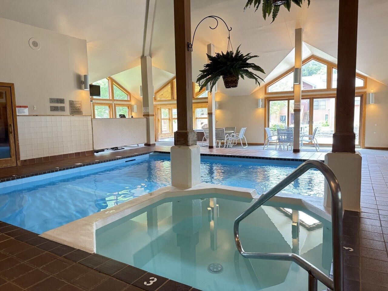 An indoor swimming pool with a separate hot tub area, clear glass walls, and a view of the outside.