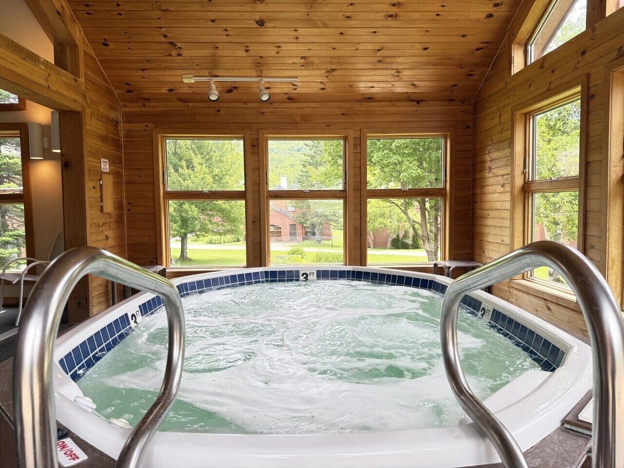 A hot tub with a view of a green landscape through large windows.