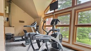 Une salle de sport équipée de tapis de course et de vélos d’exercice, dotée de grandes fenêtres et d’un téléviseur.