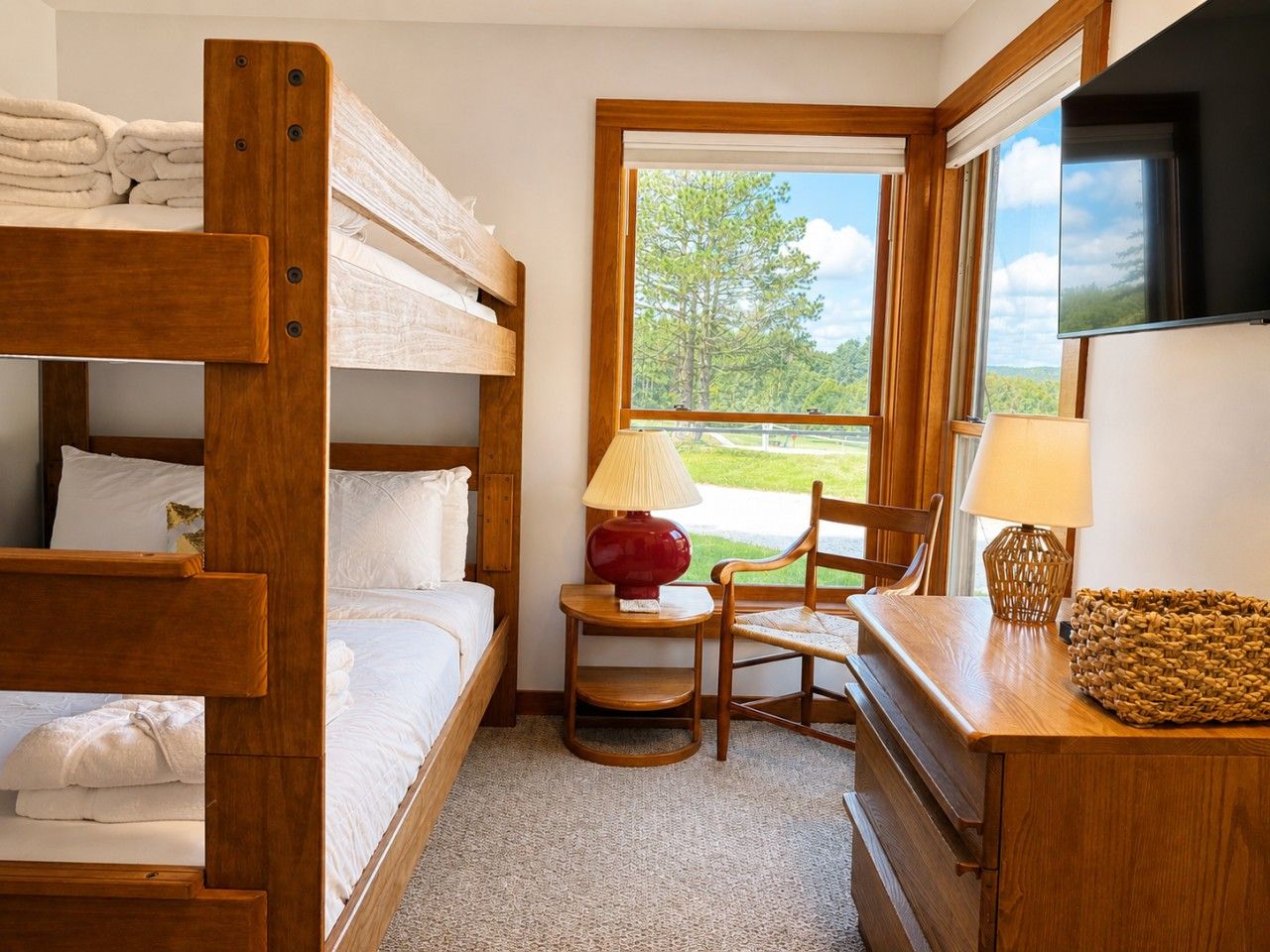 Une chambre avec des lits superposés, un bureau, une chaise, des lampes et une vue sur l’extérieur.