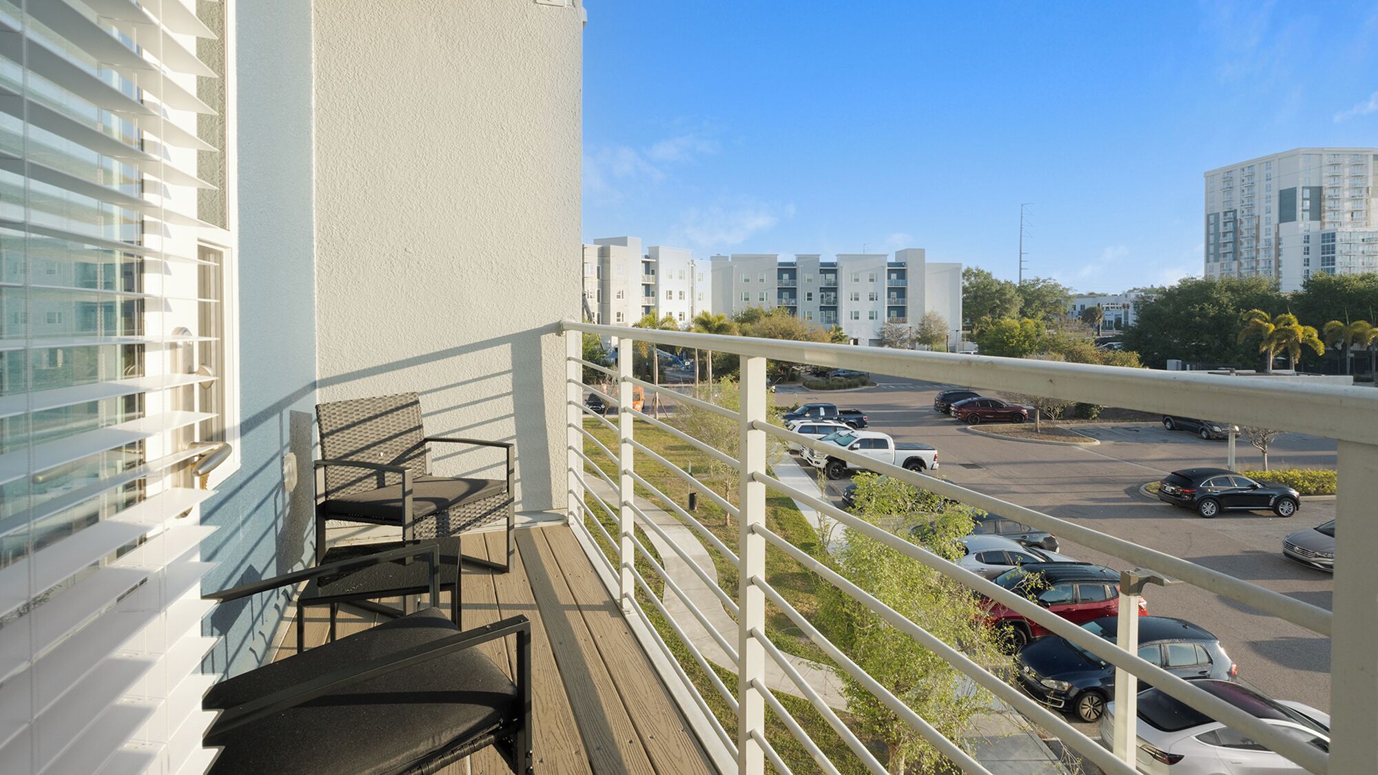 Een balkon met uitzicht op een parkeerplaats en aangrenzende gebouwen.