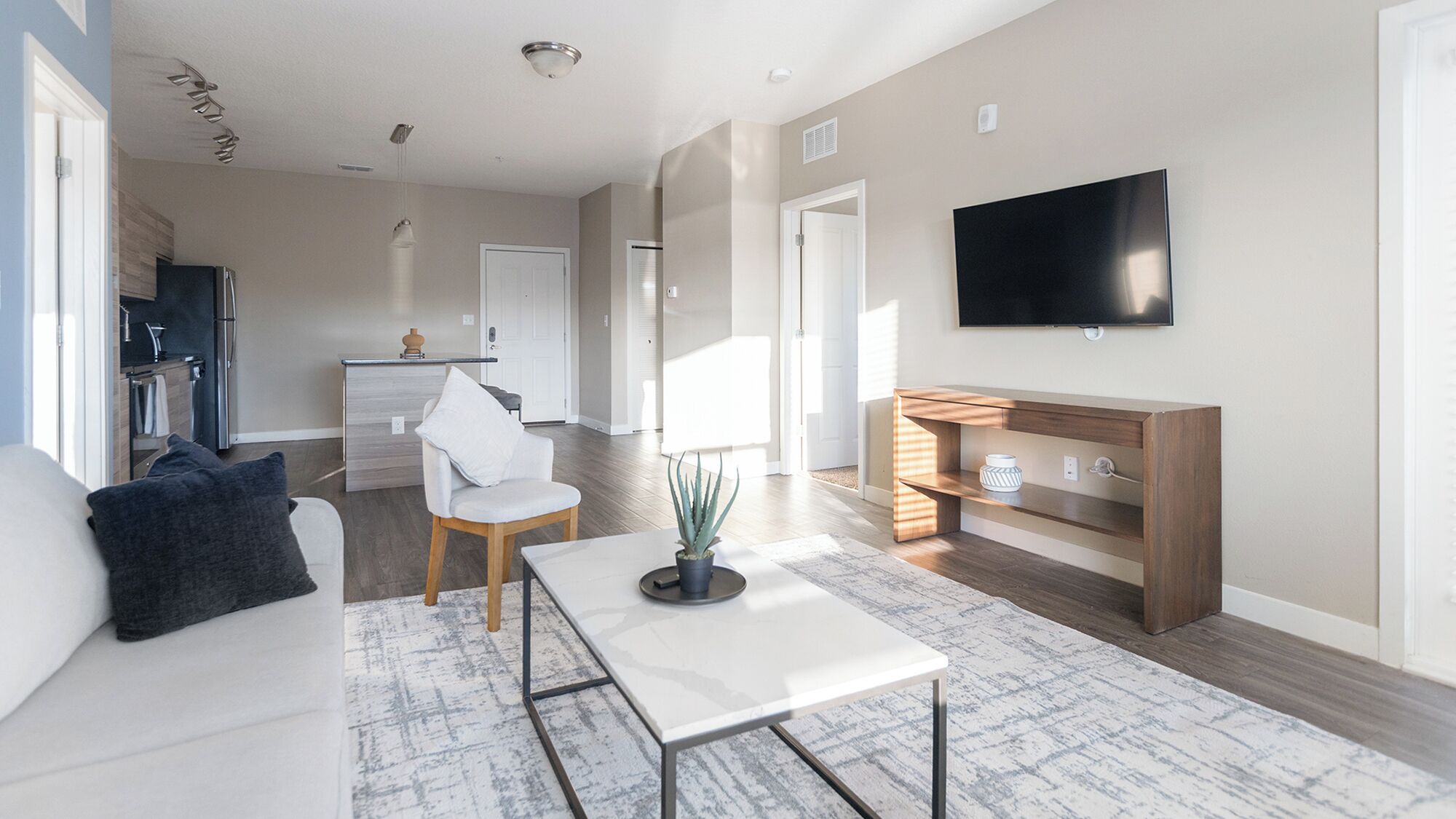 A modern living room with a sofa, coffee table, TV, and a kitchen area in the background.