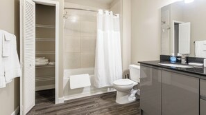 A bathroom with a shower, toilet, and a sink with a mirror. - Landing Furnished Apartments - Clearwater (Clearwater)