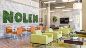 Un área de descanso moderna con pared de ladrillo, letras de follaje verde que deletrean "NOLEN" y disposición de asientos.
