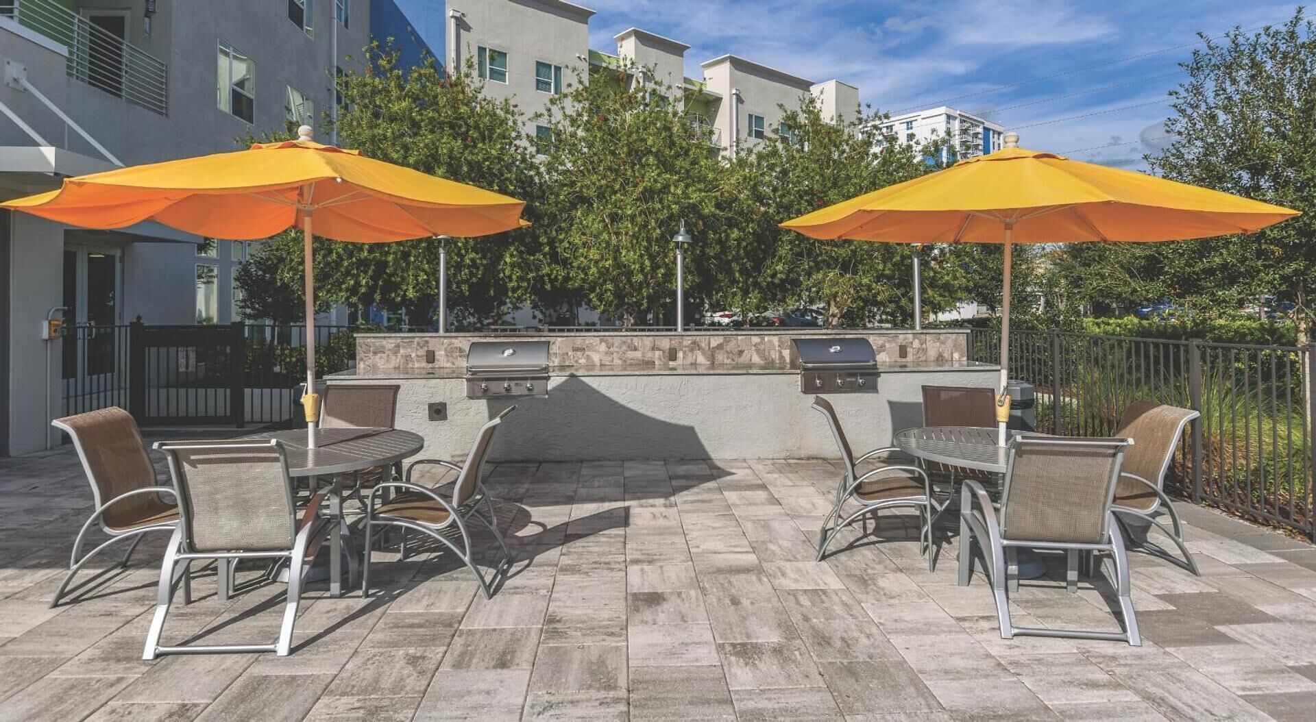 An outdoor patio with a grill, two umbrellas, and outdoor seating.